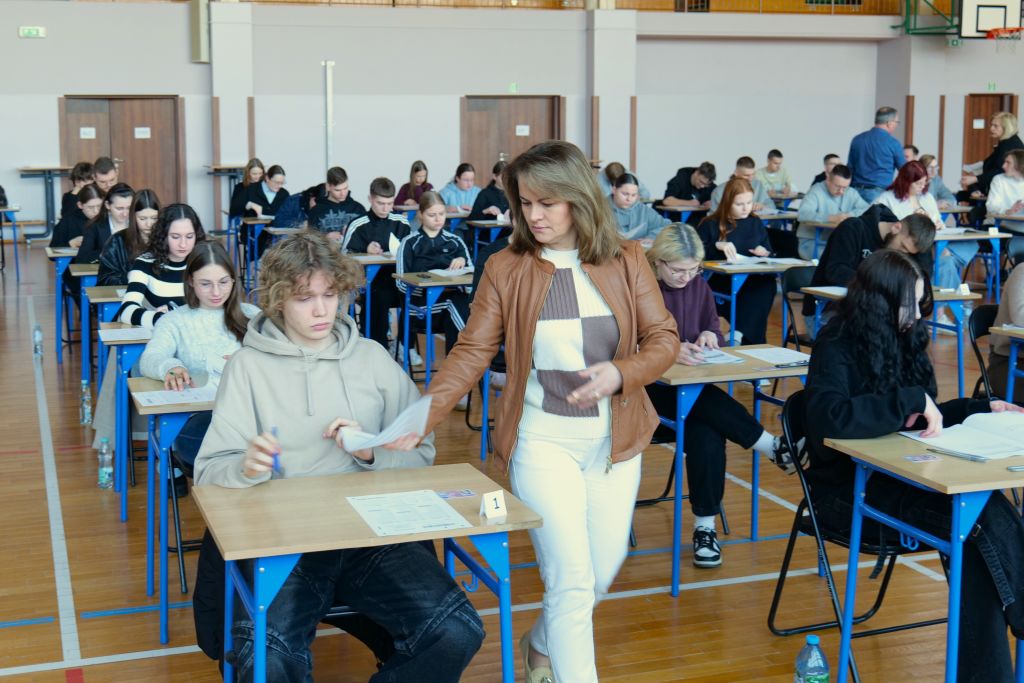 Nauczyciel nadzorujący przebieg egzaminu rozdaje arkusze zdającym